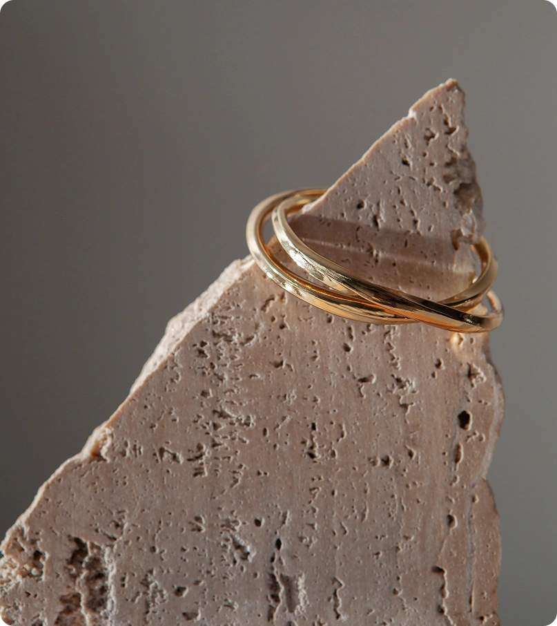 Elegante minimalistische gouden ringen tentoongesteld op een gestructureerd natuurlijk stenen oppervlak met zacht neutraal studiolicht.