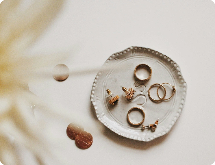 Minimalistische flat lay van elegante gouden ringen en oorbellen gerangschikt op een decoratief keramisch bord met zacht natuurlijk licht.