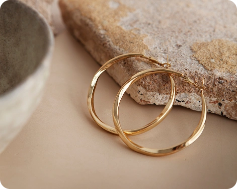 Minimalistische gouden creolen geplaatst op een natuurlijk stenen oppervlak met warme neutrale tinten en elegante zachte verlichting.