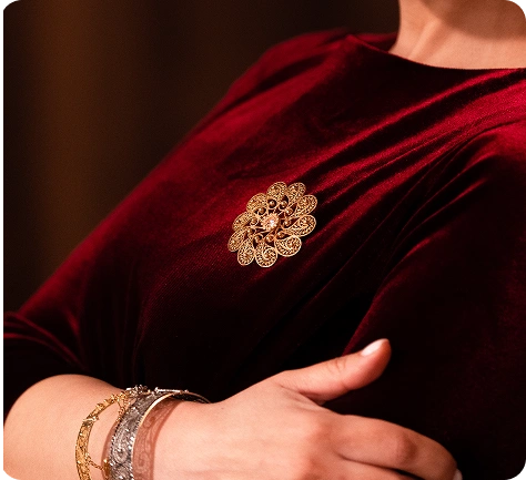 Vrouw die een elegante gouden oosters-stijl broche draagt op een diep rode fluwelen jurk, gecombineerd met luxe armbanden en accessoires.